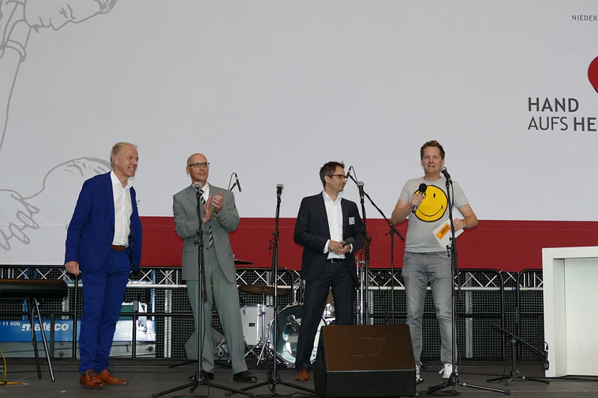 Foto von Malte Janssen, Radiomoderator von Bremen Vier, der auf der Bühne ein Interview unter anderem mit dem Geschäftsführer der Unfallkasse Bremen, Sven Broska, führt